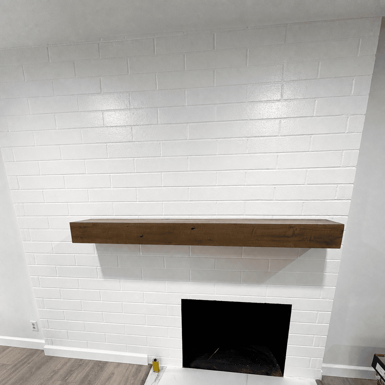 Painted-brick fireplace with a floating wood mantel after interior remodel
